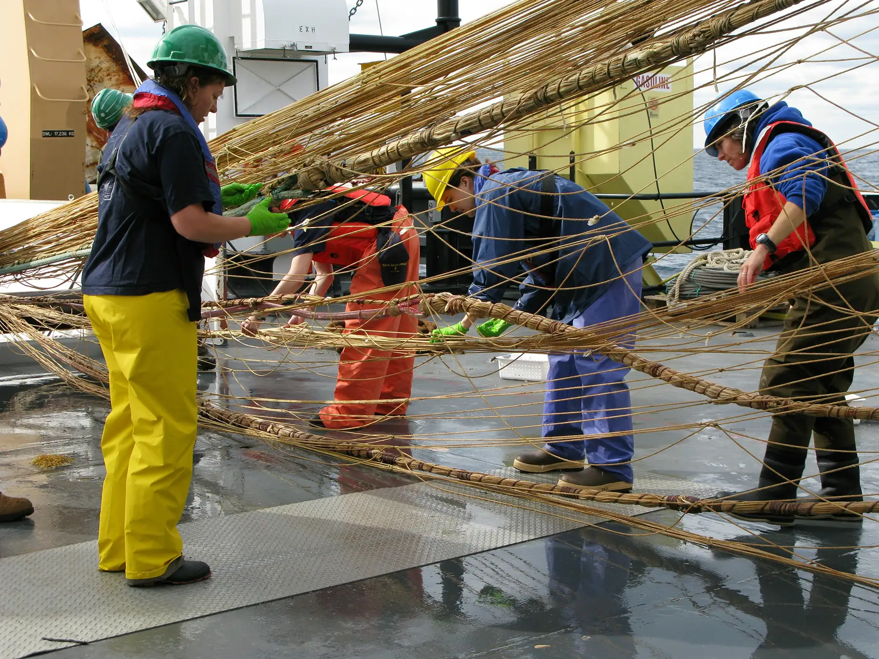 Fishers working on trawling net on a ship.